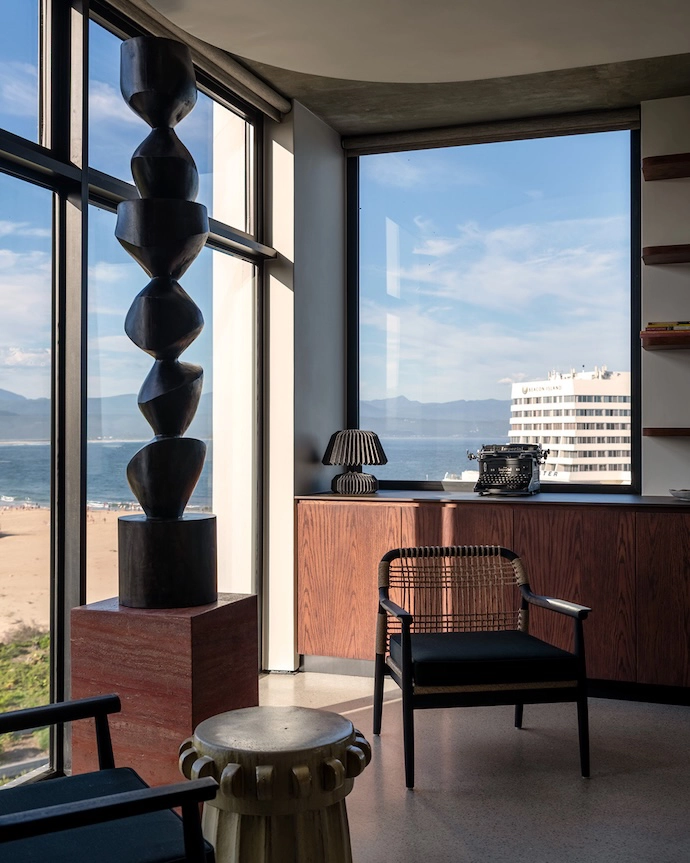 Occasional chairs and a stone sidetable from Weylandts are arranged to take in the view of Robberg Beach, and of Beacon Island Hotel past the owner’s antique typewriter.